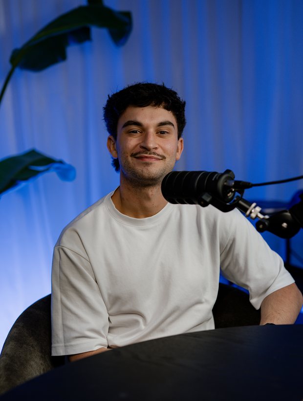 Bailey Williams seated at the studio table in front of a microphone, smiling.